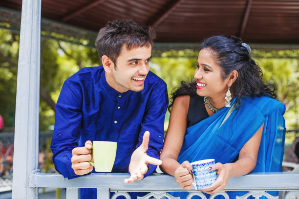 Beautiful Indian couple wearing traditional clothes drinking coffee or tea on a balcony and talking